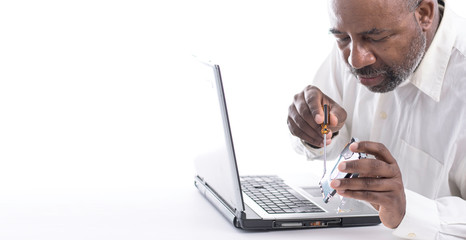 African American Male technician holding hard drive in front of computer laptop