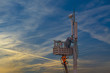 Uniformed worker repairing cellular tower against the sky at sunset