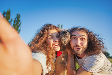 Wall Mural - couple playing with dog in park, man and woman happy family together, making selfie photo