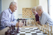 © Seventyfour - Old man in checked shirt playing chess with two focused schoolchildren studying at chess club