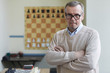 Aged male principal of chess club posing for pictures for advertising chess classes for schoolchildren