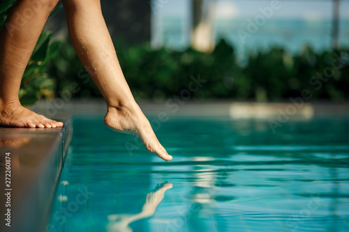 Closeup young female leg touch blue water in swimming pool Poster Mural XXL