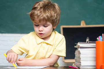 Elementary school and education - school concept. Cute little preschool kid boy in a classroom. Kids gets ready for school. Cheerful smiling little pupil having fun against blackboard.