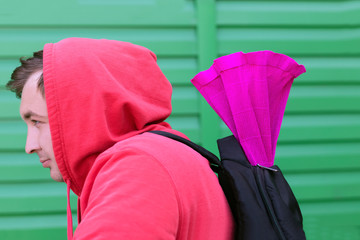 A young man in a red jacket with a hood on his head and a backpack on his back carries a gift in a bright package to his girlfriend.