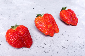 Wall Mural - Three ugly strawberries are lying diagonally on grey concrete background. 