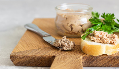 Wall Mural - Liver pate in a glass jar with fresh bread and parsley on a wooden cutting board. Light grey stone background.