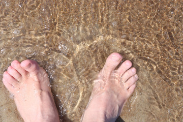 Woman feet on sea sand in soft wave water. Barefoot on beach top view.