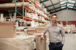Manager smiling while leaning against stock in a large warehouse