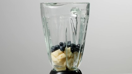 Wall Mural - Mixing fruit in a blender. Grey background. Slow motion.