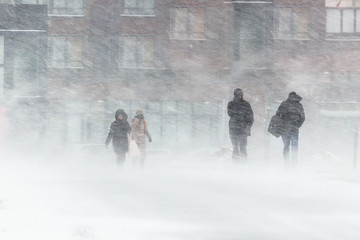 The blizzard, strong wind, sleet, against the background of houses blurred silhouettes of people, they try to hide from bad weather, overcome all difficulties of severe climate. go to the bus stop