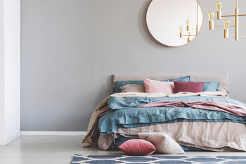 Wall Mural - Chick round mirror on grey empty copy space wall in elegant bedroom interior with warm bed with blue, pastel pink and beige bedding