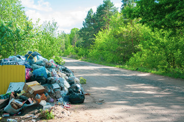 Illegal dump near the country sand road in the country on sunny day. Trash pollution in the nature. Dirty dump near the forest woods