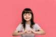 © Marharyta Hanhalo - Smiling little girl in grey blank t-shirt showing heart with two hands, love sign. Isolated over pink background. Smiling lovely cute child showing heart gesture with fingers