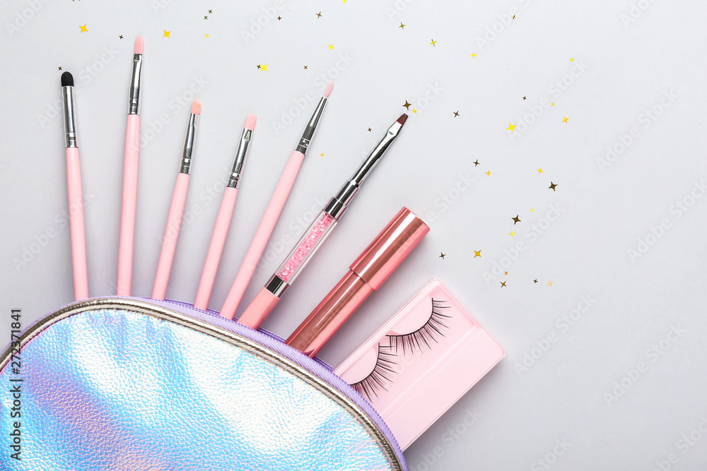 Cosmetic bag with brushes, lipstick and fake eyelashes on light background
