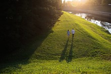 Young Couple Is Walking Along The River Bank At Sunset.