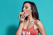 © G-Stock Faces - So tasty! Beautiful young woman in swimwear eating donut while standing against blue background