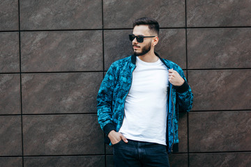 Wall Mural - A young stylish man with a beard in a white T-shirt and glasses. Street photo