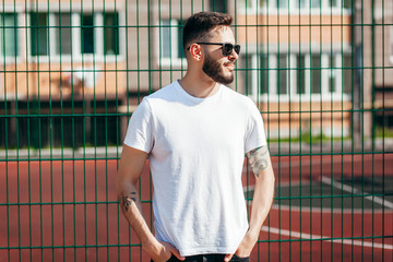 Wall Mural - A young stylish man with a beard in a white T-shirt and glasses. Street photo