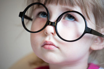 serious white child girl in big black glasses face closeup portrait