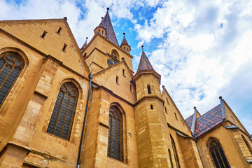 Gothic-style Lutheran Cathedral of Saint Mary (Catedrala Evanghelica C.A. Sfanta Maria / Evangelische Stadtpfarrkirche) in Sibiu, Romania - low angle with beautiful white clouds and blue sky.