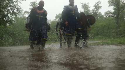 Wall Mural - Battle squad of medieval knights of the Crusaders goes in armor and with swords through a puddle on a forest road in the rain.