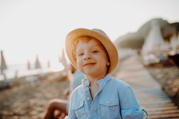 A small toddler boy standing on beach on summer holiday at sunset.