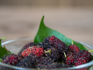 Close up of mulberry with a green leaves in Glass bowl on the wooden plate on wooden table. Mulberry this a fruit and can be eaten in have a red and purple color and delicious and sweet nature.