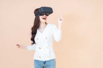 portrait of a young asia woman wearing a white cardigan and VR glasses. She is amazed by what she is seeing. Virtual reality headset. isolated orange background