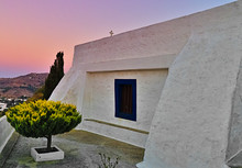 Lang="x-default" Beautiful White Chapel With Blue Window And Sort Tree At Sunset Time, Patmos Island, Greece.