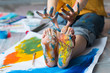 © golubovy - Fun leisure. Cropped shot of artist sitting on floor, showing feet and hands dirty with multicolor paint. Blur background.