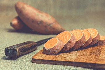 Wall Mural - Sliced raw sweet potatoes on a wooden cutting board and jute backgroud. Product photo of batats. Healthy diet for vegetarians and vegans. Source of vitamins. Wooden plank with batatas and knife