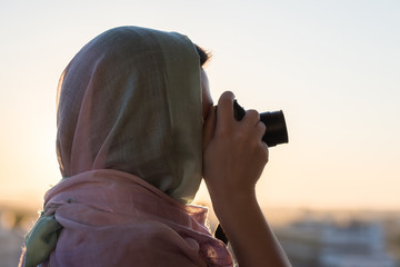 Wall Mural - Arab Woman Photographer in a scarf taking picture using Camera on the sunset background. Halal travel concept