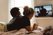 © Chelsea Victoria/Stocksy - Two female friends hanging out in bed and watching tv
