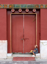 Pretty Asian Little Girl Sitting In Front Of The Old Palace Gate. Ancient Architecture Wall Background