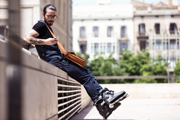 Hipster young man using his mobile phone while sitting in the street.