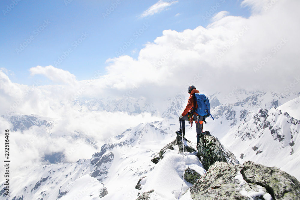 mountaineer on the top of a mountain in the background of the landscape of snowy mountains - obrazy, fototapety, plakaty 
