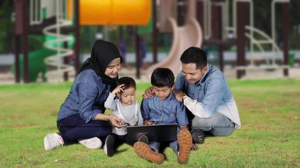 Sticker - Happy children and their parents using a laptop computer while sitting on the grass at the park. Shot in 4k resolution