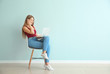 © Pixel-Shot - Beautiful young woman with laptop sitting on chair against color wall