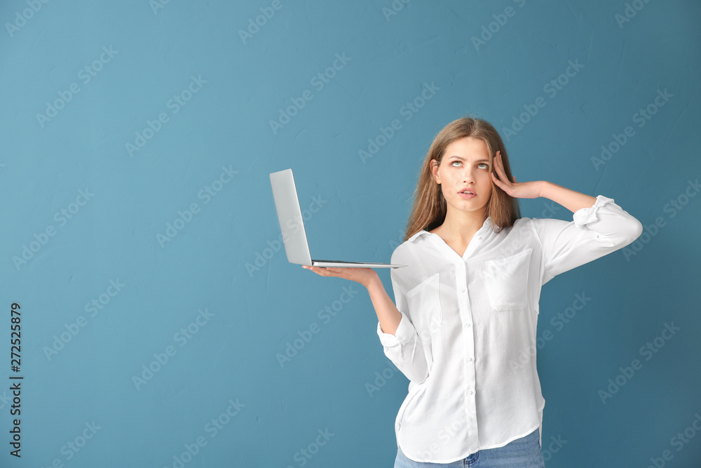 Thoughtful young woman with laptop on color background