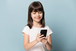 © fizkes - Little girl using smart phone posing isolated on blue background