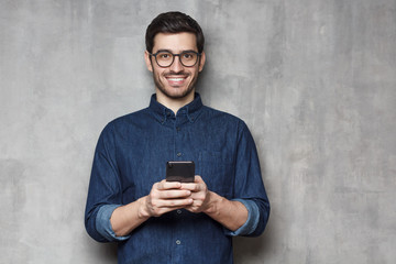 Caucasian male in glasses holding smartphone and looking at camera, isolated