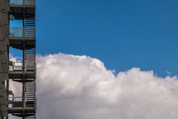 Business building with metal emergency ladder / fire escape in modern office buildings with repeating structure and reflected sky and clouds.