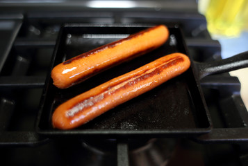 Wall Mural - Hotdogs cooking on a raclette pan on a natural gas stove.