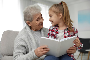 Canvas Print - Cute girl and her grandmother reading book at home