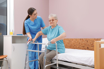 Sticker - Nurse assisting senior woman with walker to get up from bed in hospital ward