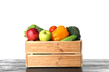 Wooden crate filled with fresh vegetables and apples on table against white background