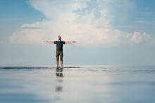 A Man Stands In Shallow Water. His Hands Are Raised