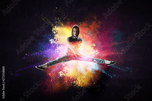 Modern female dancer jumping in hoodie with colourful splashes background. Mi...