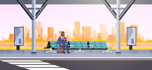 Wall Mural - businessman sitting modern bus stop african american business man with suitcase waiting public transport on airport station cityscape background flat horizontal full length