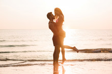 Couple In Love Having Romantic Tender Moments At Sunset On The Beach - Young Lovers Enjoying Summer Vacation - Love, Travel And Relationship Concept - Focus On Bodies Silhouette